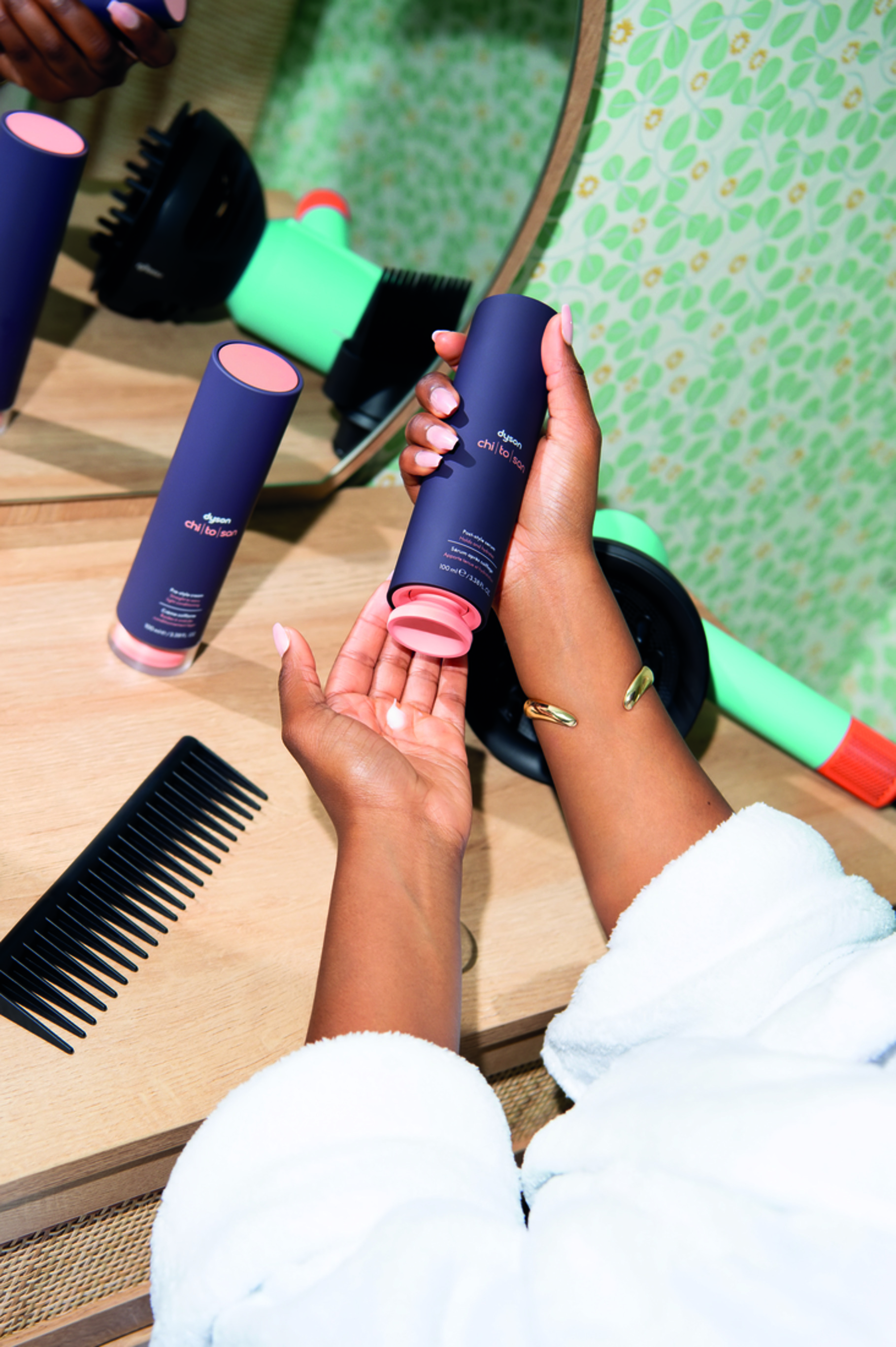 A model holds a bottle of Dyson Chitosan Post-style serum as they style their hair.